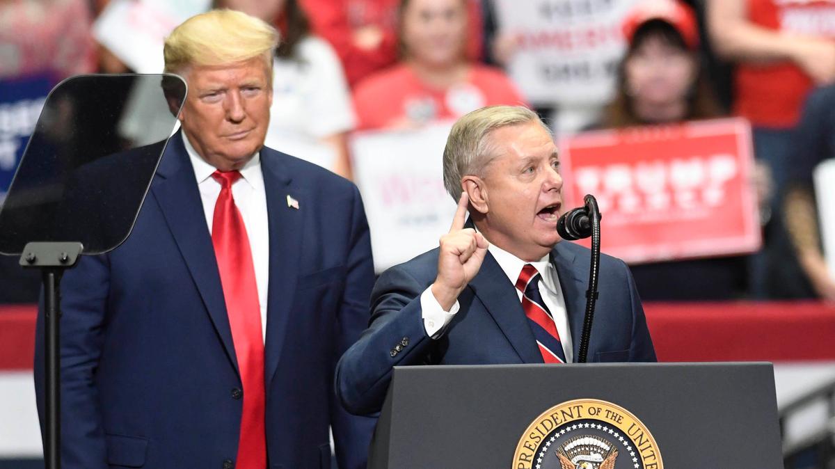Then-President Donald Trump listens as U.S. Senator Lindsey Graham of South Carolina addresses supporters during a rally at Bojangles Arena in Charlotte, NC on March 2, 2020.