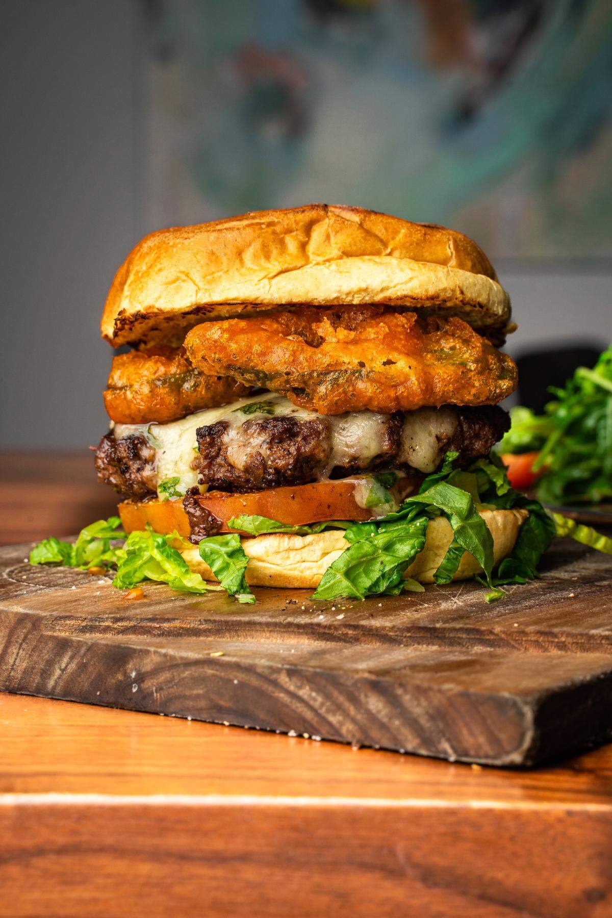 The Alchemy Steak Burger is topped with heirloom tomato, romaine lettuce, plant based white cheddar, tempura jalapenos and tomato aioli.