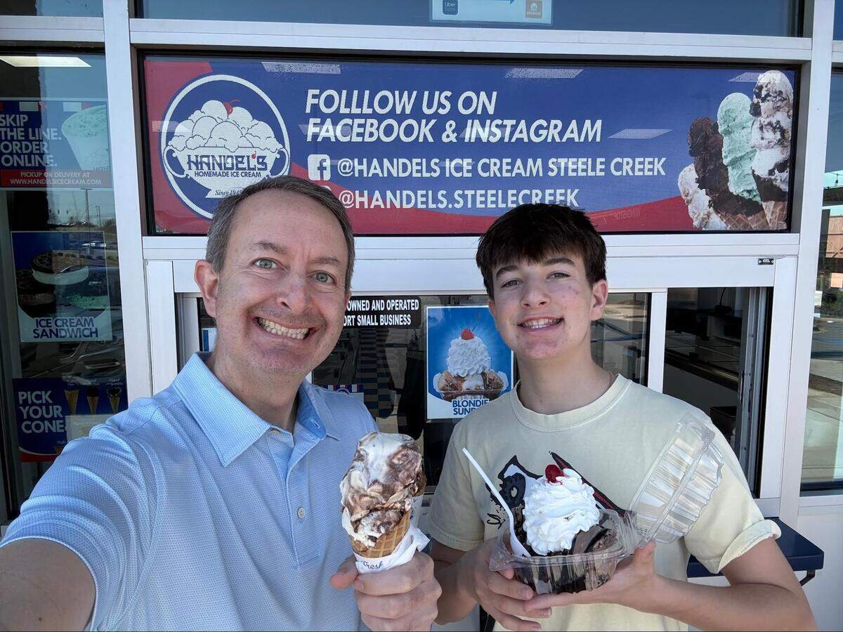 A parent and child smile outside a Handel’s Homemade Ice Cream walk-up window while holding their treats.