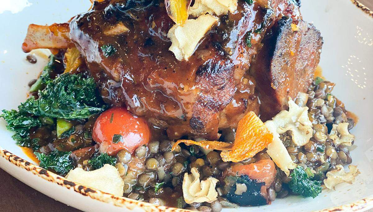 The Crunkelton's Pork Shank is a 16-hour confit Kurobuta pork dish served over lentil tabbouleh with hearth vegetables and topped with hot honey harissa and taro chips.