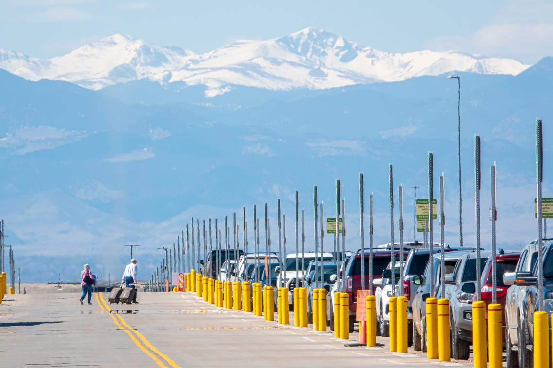 Passengers haul luggage across the street to a parking lot at Denver International Airport.