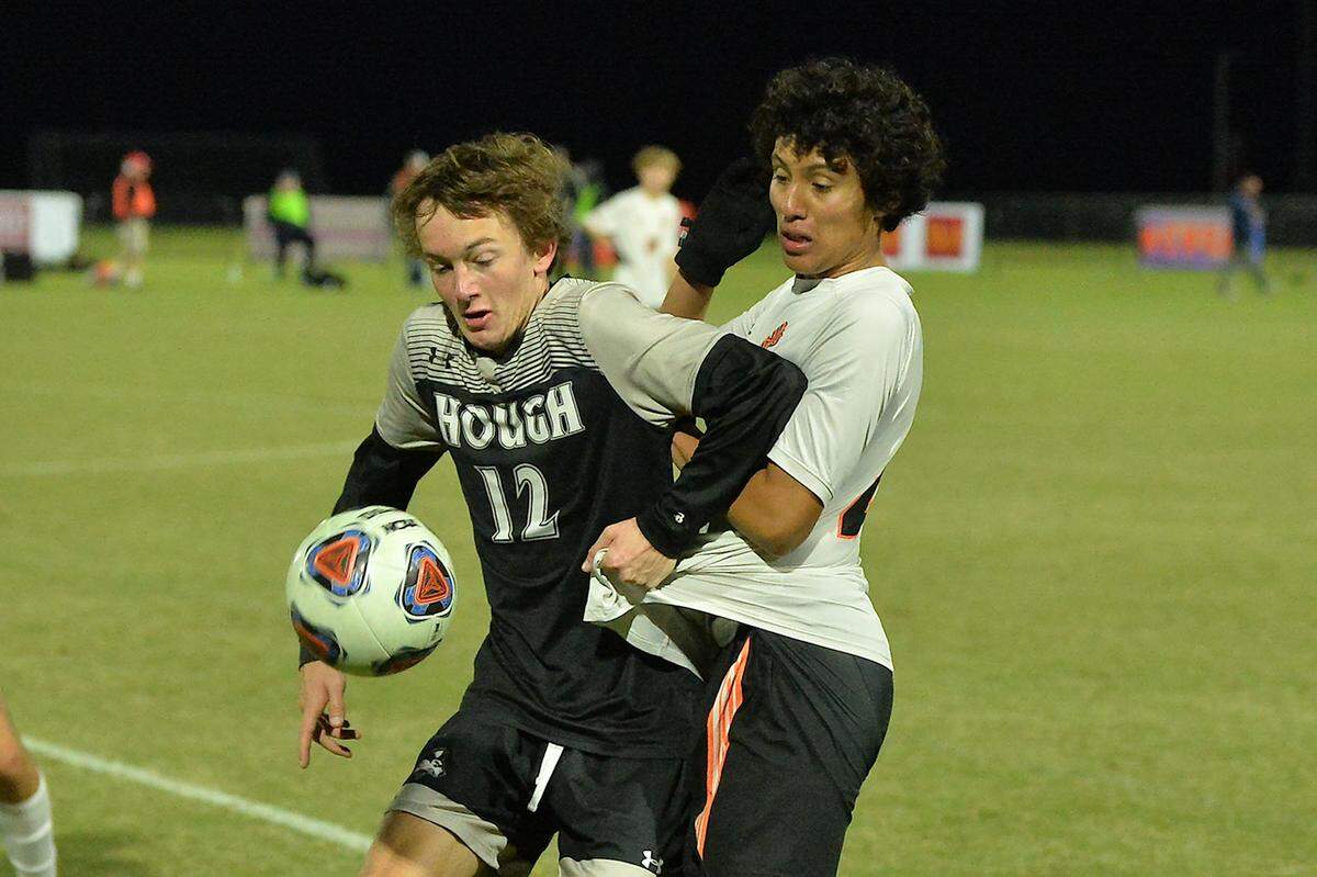 Hough’s Nicolas Patrignani (12) defends the ball from New Hanover’s Luis Miranda (8) during the first half. The New Hanover Wildcats and the Hough Huskies met in the NCHSAA 4A Boys Soccer Championships in Cary, N.C. on November 20, 2021.
