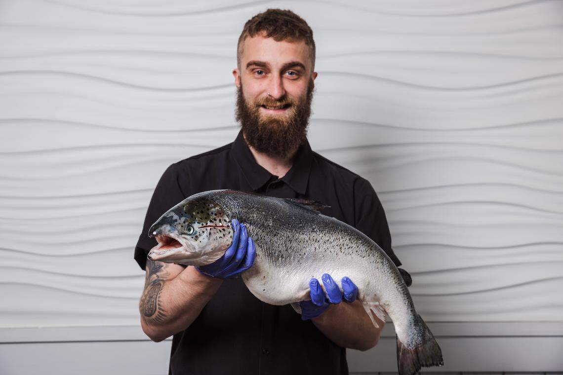 Chef Jonathan Cox holds a giant fish in front of a white wall with a wavy pattern.