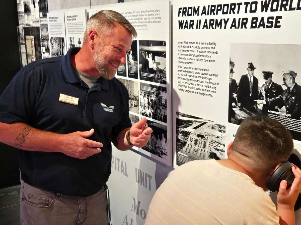 Jason Rivenbark, a facility operator at the Sullenberger Aviation Museum, educates a visitor about an air raid siren used by U.S. Army at the airport during World War II.