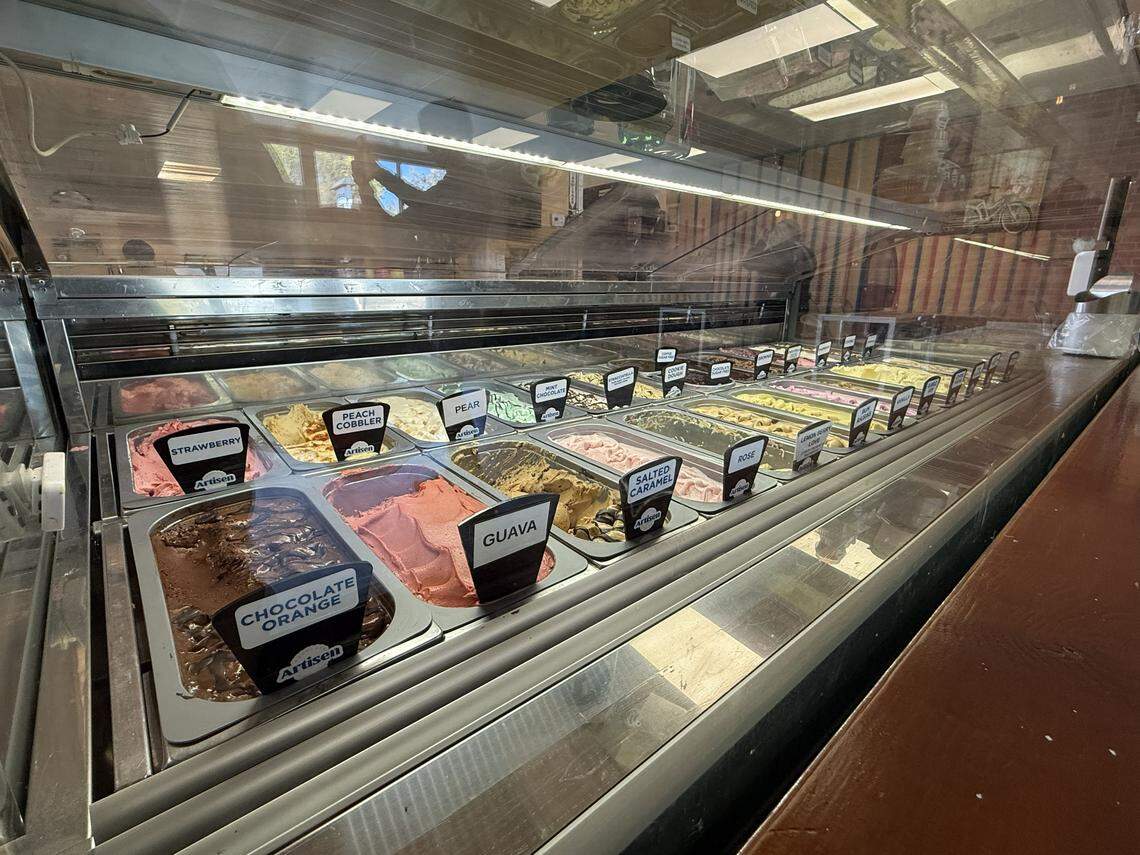 A wide view of a clean, glass-fronted display case filled with rows of colorful vegelato. Each metal bin features a black label identifying unique flavors such as Chocolate Orange, Guava, Salted Caramel, Rose, and Pear. The vibrant scoops are perfectly swirled, inviting customers to choose from a diverse palette of handcrafted frozen desserts.
