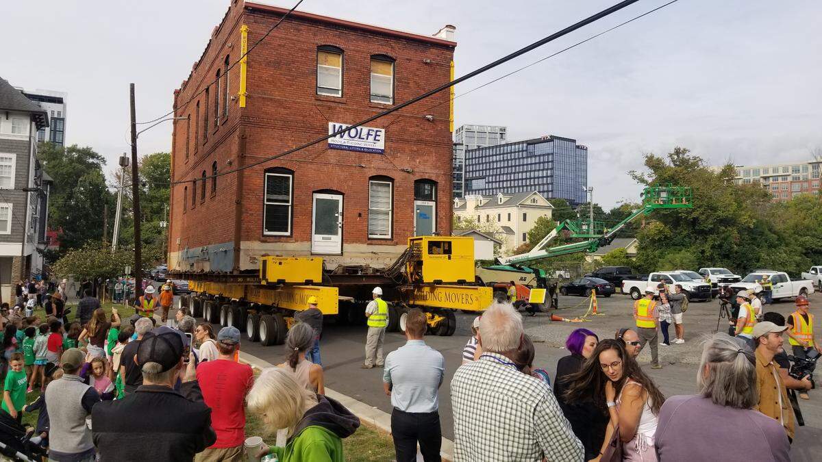 The historic Leeper & Wyatt building is moved up the street by construction crews as community members watch.