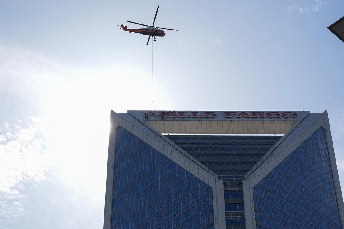 A helicopter hoists letters as workers guide them into place on the top of the Wells Fargo building in uptown, Sunday, June 15, 2025, in Charlotte, N.C.