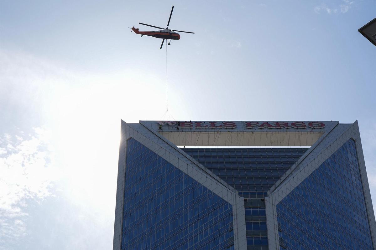 A helicopter hoists letters as workers guide them into place on the top of the Wells Fargo building in uptown, Sunday, June 15.