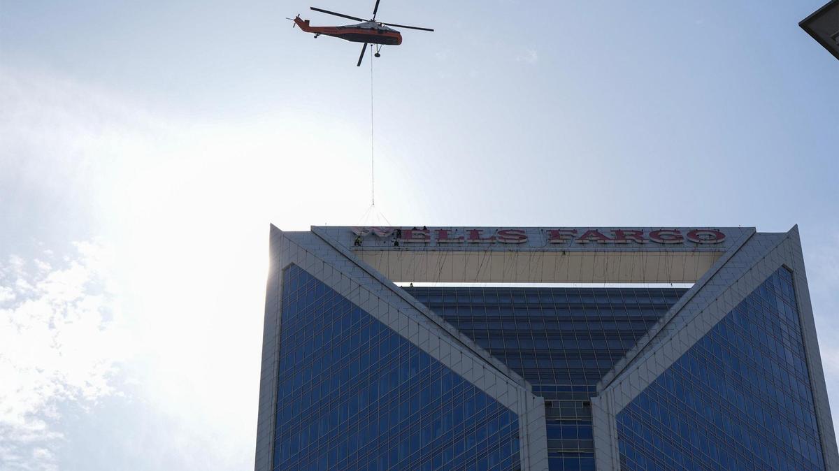 A helicopter hoists letters as workers guide them into place on the top of the Wells Fargo building in uptown, Sunday, June 15, 2025, in Charlotte, N.C.