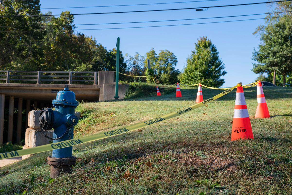 Caution tape and cones from the City of Charlotte’s water department close off a portion of the area surrounding the site of a water main break on Tuesday, October 19, 2021 in Charlotte, NC. On Monday, water was seen gushing from this area under the bridge in the 1400 block of Remount Road.
