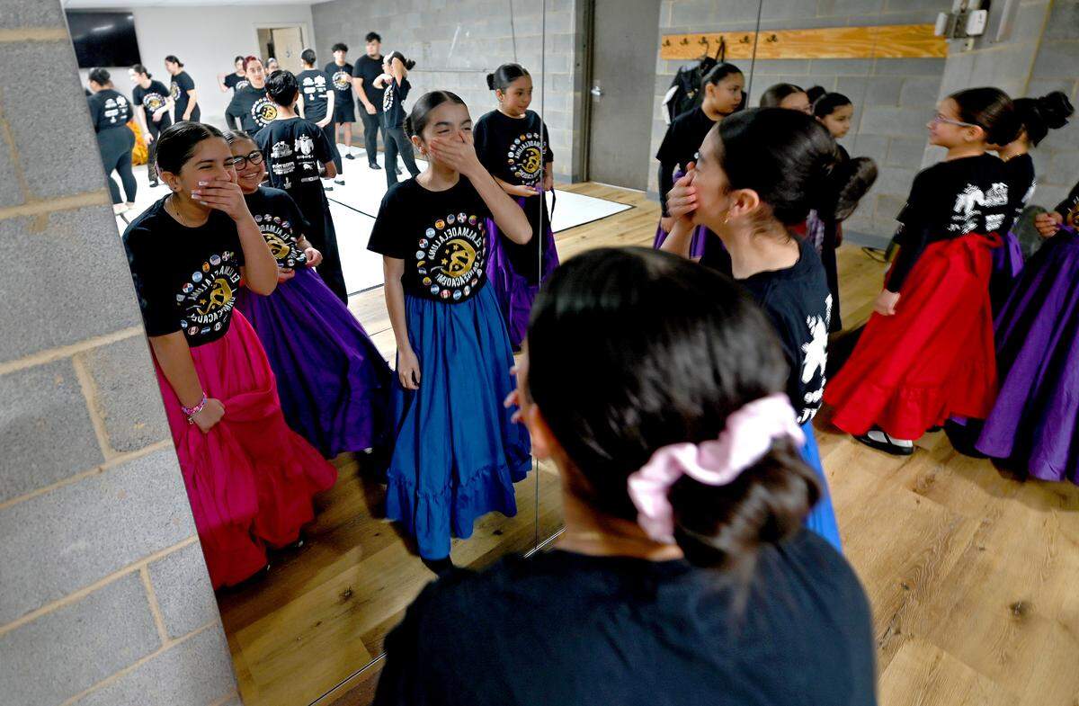 Young members of the dance troupe El Alma de la Luna shyly laugh behind their hands as they look into a mirror in the studio.