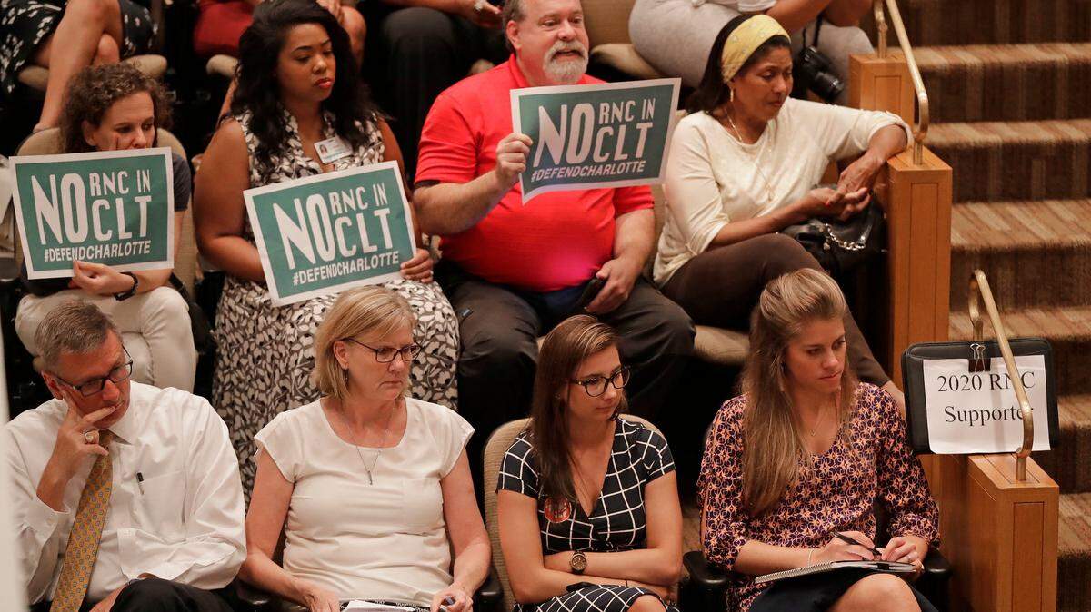 People hold signs for and against the Republican National Convention during a Charlotte City Council forum this month.