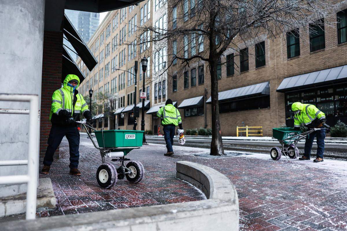 Men spread salt on the 5th Street sidewalk after rain, snow and sleet fell overnight on Sunday, January 25, 2026.