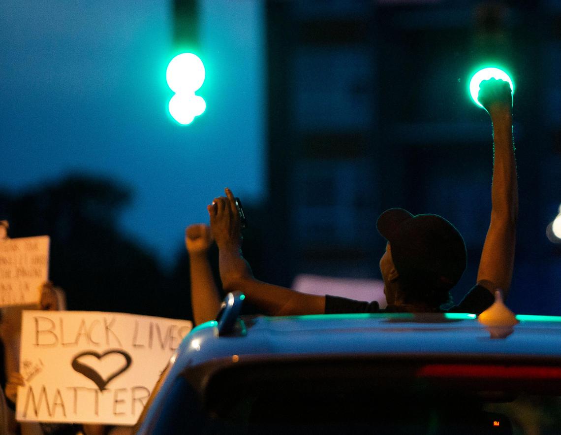 A protester raises their fist as demonstrators march by her car in Charlotte, NC on Friday, June 5, 2020.