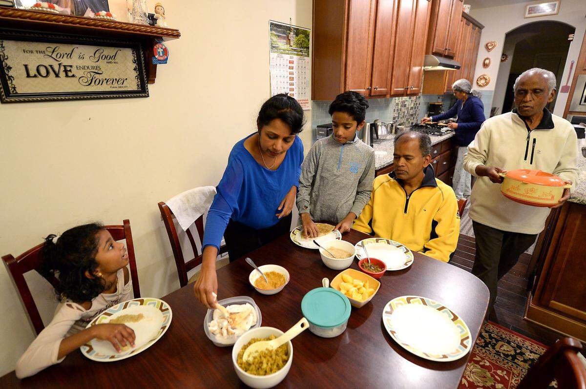 Nidiya Gaspar, center, places food onto her children Nila, left, and Neal’s plates as her father Lourdu Susai looks on. The Gaspar family is one of millions of multigenerational households in the United States.