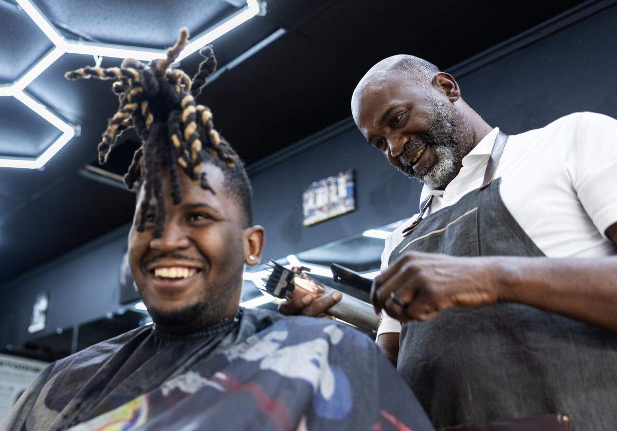 Brian Mack, right, cuts his son’s hair, B.J., at House of Hoops Barbershop in Charlotte, N.C., on Monday, July 1, 2024. B.J. uses NIL money for dad to open barber shop in Charlotte