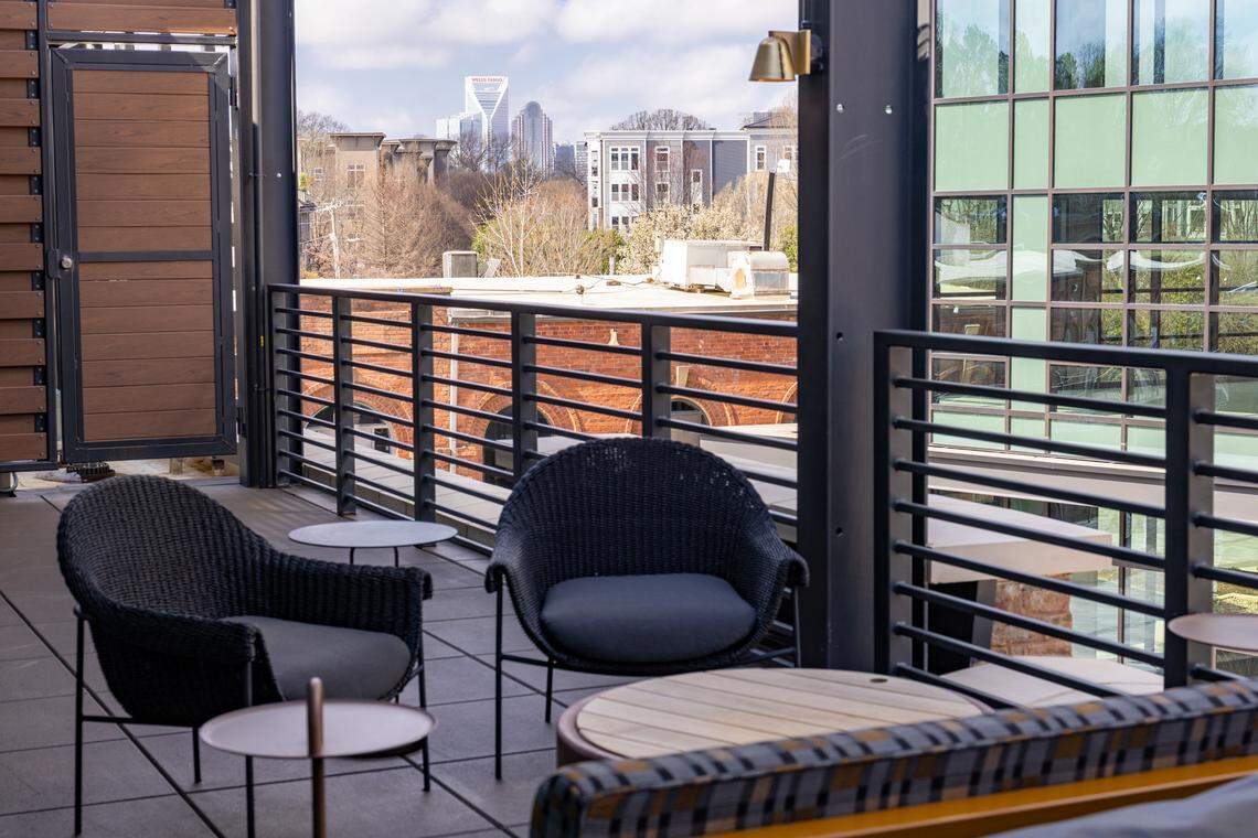 A terrace overlooks a bustling street and modern multi-story brick and glass buildings. A vibrant, large-scale floral mural is visible on a neighboring wall, and a city skyline is visible in the distance.