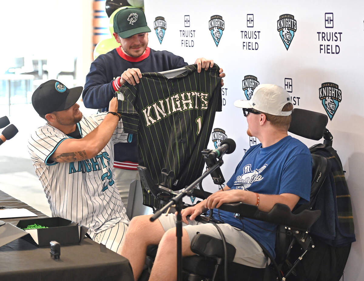 Charlotte Knights manager Chad Pinder, left, and graphic designer Will Briggs, center, show Nick Adair his custom jersey design during a news conference at Truist Field in Charlotte, North Carolina, on Saturday, June 27, 2026.