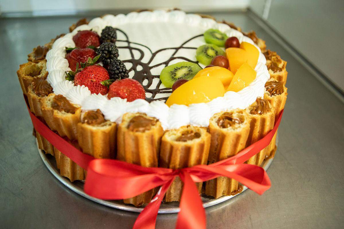 A cake adorned with fresh fruit and surrounded by sections of dulce-de-leche-filled churros, is held together with a red ribbon as it sits in a refrigerated case inside Manolo’s Bakery on Central Avenue on Tuesday, June 17, 2022 in Charlotte, NC.