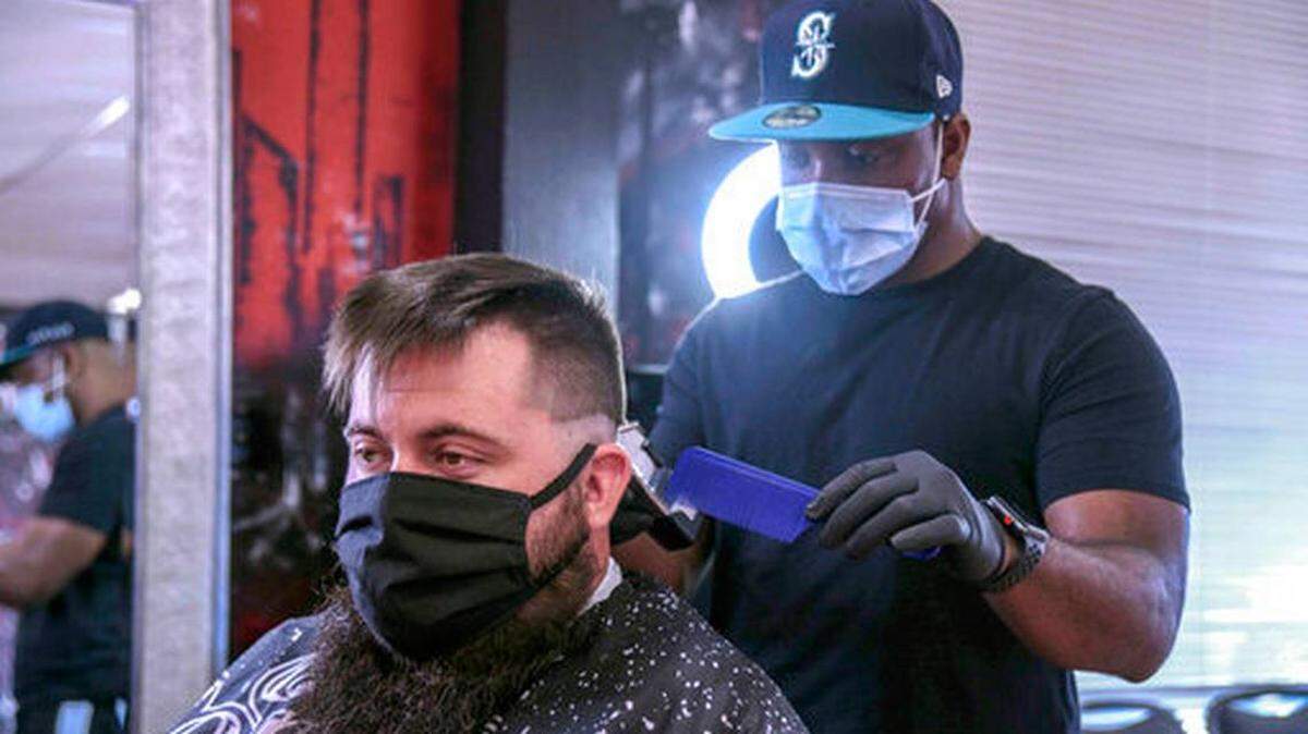 Barber Kola Peavy trims customer Aaron Bolling’s hair in Hattiesburg, Miss., while both wear masks. Some cities are mandating face masks in public and issuing fines to slow the spread of coronavirus.