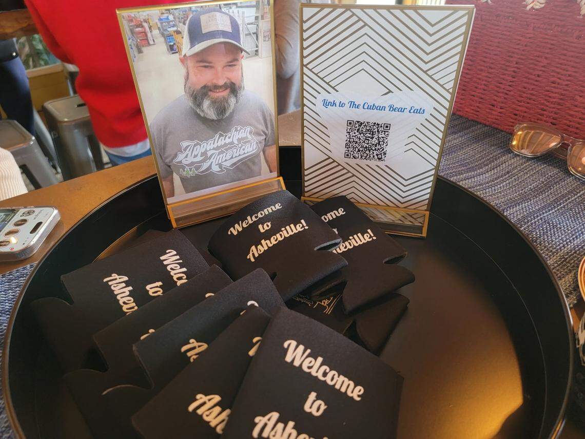“Welcome to Asheville!” beer cozies share a tray with a photo of Tony Prieto and a QR code directing guests to a CharlotteFive story on his community fame.