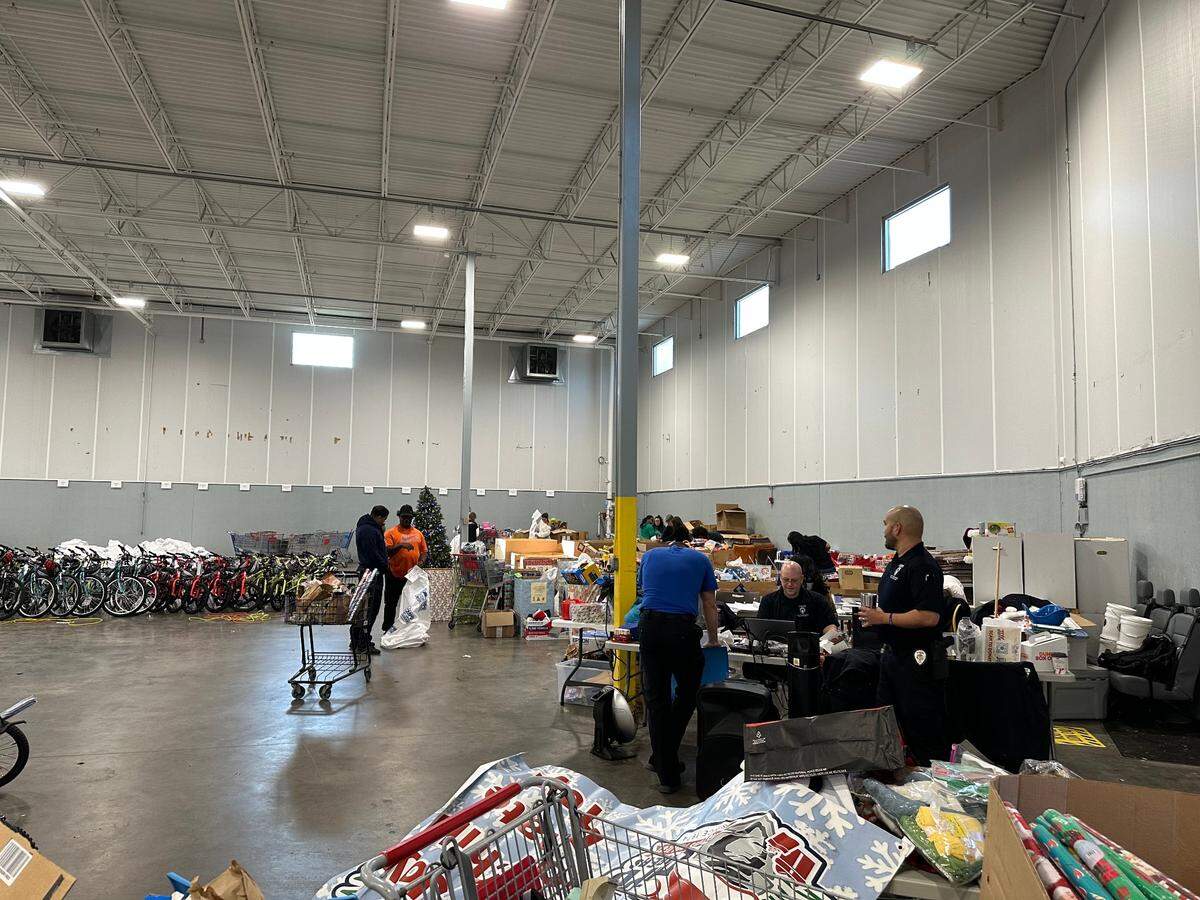 Officer Ryan Botzenmayer, left, sitting at a table near the gifts that volunteers would put in bags for deliveries. Officer Francis Auayang, right, stands nearby.