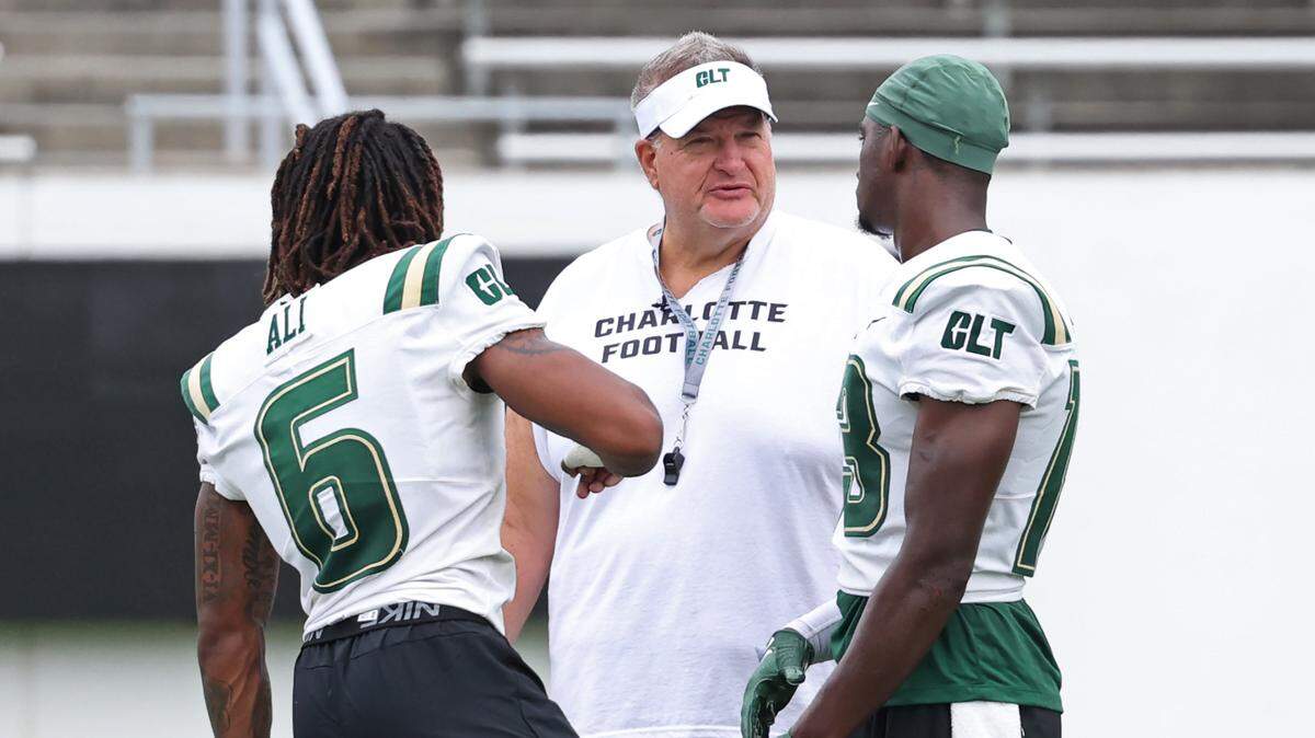 Charlotte 49ers head football coach Biff Poggi, center, speaks with two of his players during the team’s first practice on Friday, August 4, 2023.