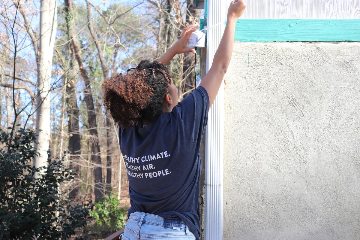 Daisha Wall of CleanAIRE NC arranges an air monitor on a home. The devices check real-time air quality data which is shown on an interactive online map.