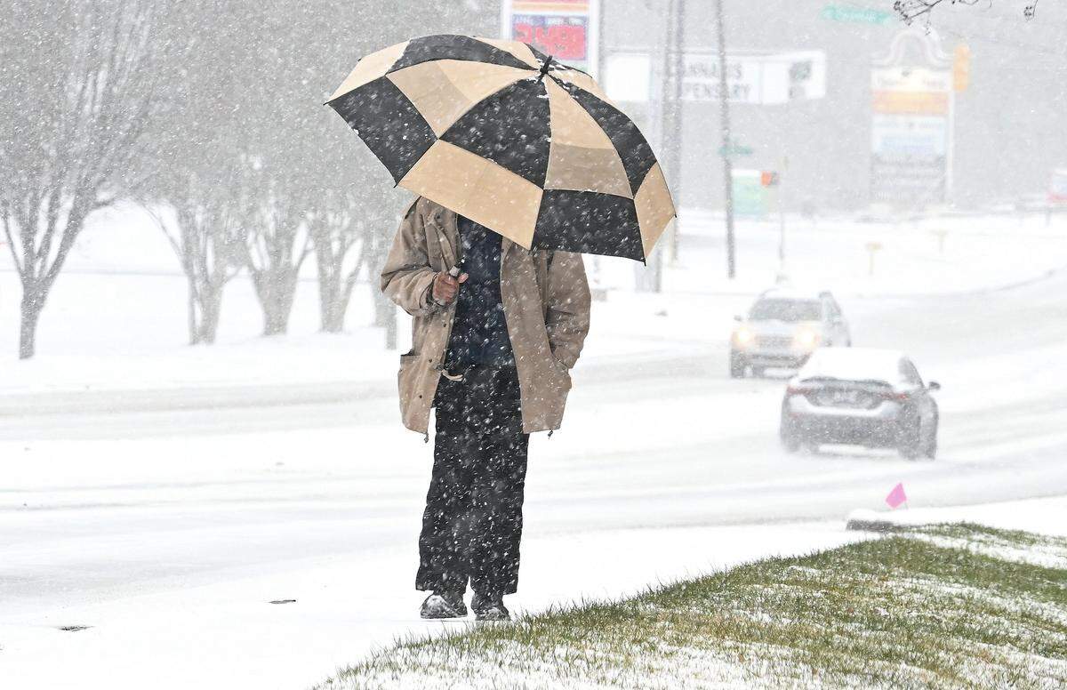 Calvin Suggs shields himself from the falling snow with an umbrella as he walks along Monroe Road in Charlotte, NC on Saturday, January 31, 2026.