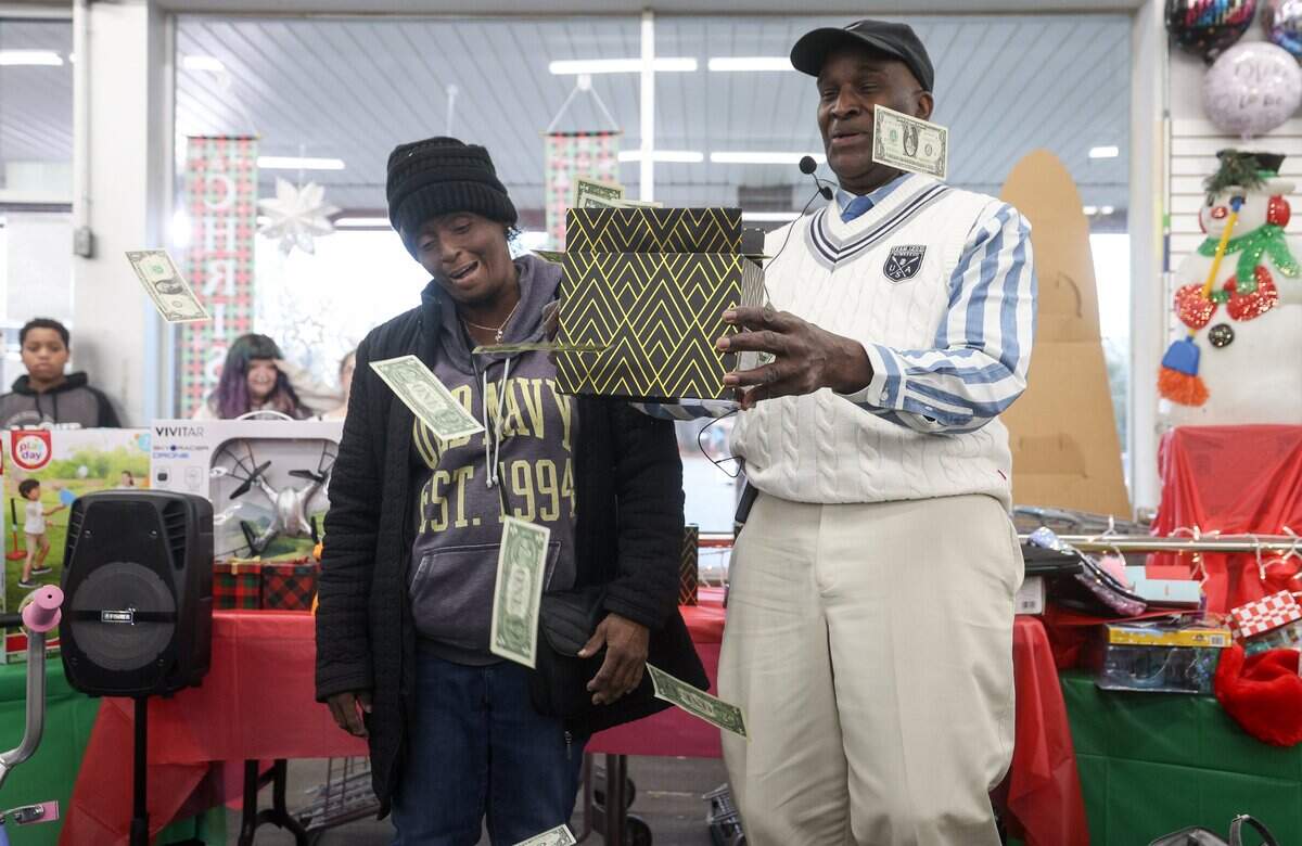 Vondetta Davis, left, is surprised with dollar bills shooting out of a gift box held by Tim Greene, one of the hosts of a “secret santa” gift giveaway at Might Dollar store in Gastonia, NC on Friday, December 12, 2025.
