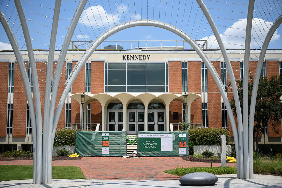 The Kennedy Building stands behind a construction barrier on UNC Charlotte’s campus. Directly adjacent to the building is the Constellation Garden Memorial.