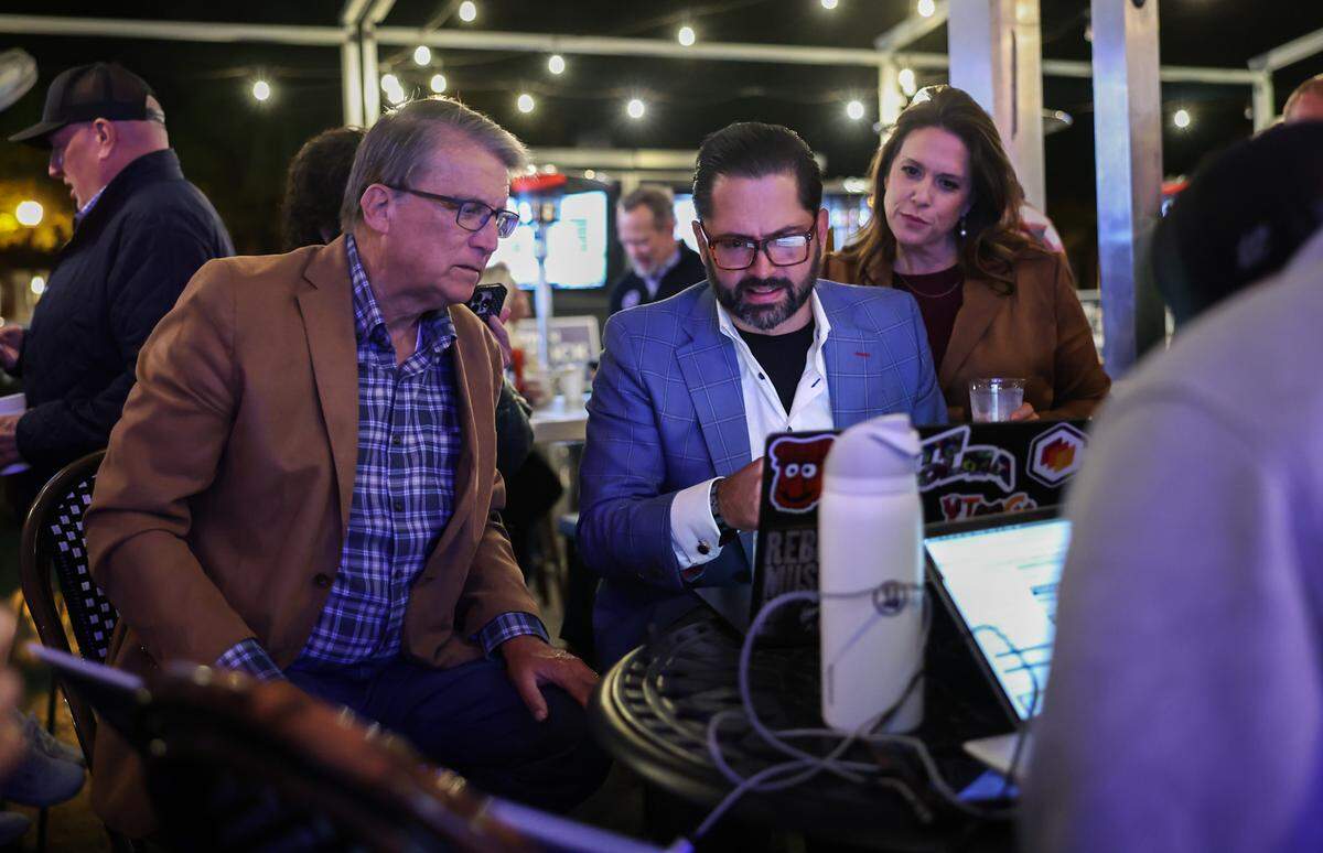 Former Governor Pat McCrory, left, Tariq Bokhari and his wife, Krista, check election results during a watch party at Selwyn Avenue Pub in Charlotte.