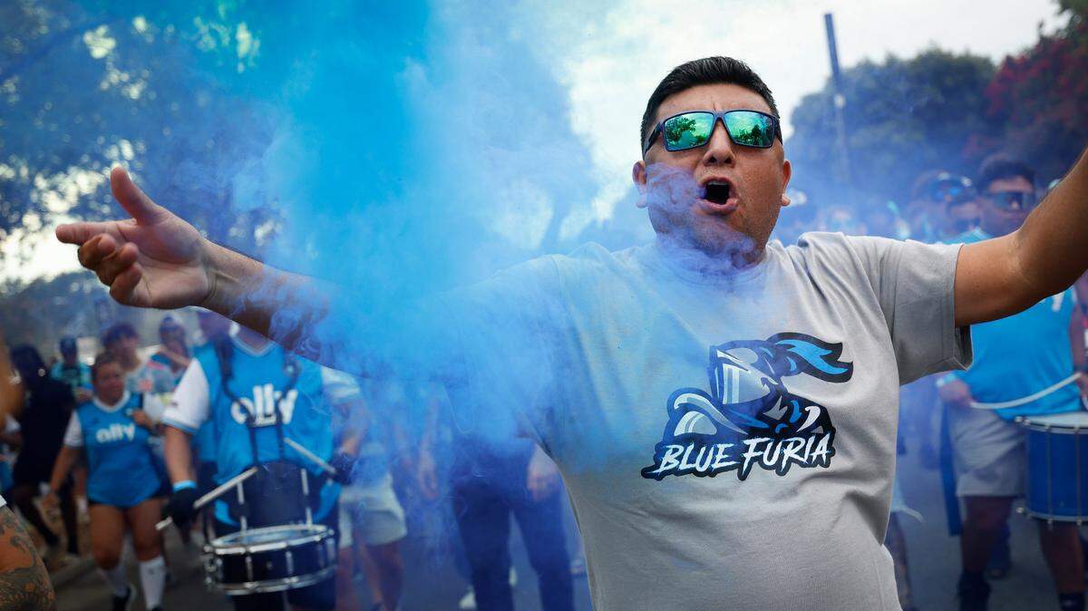 Arturo Vasquez, of Charlotte, N.C., walks through colored smoke while marching with other fans before a game between Charlotte FC and Columbus Crew at Bank of America Stadium in Charlotte, N.C., Saturday, July 30, 2022.