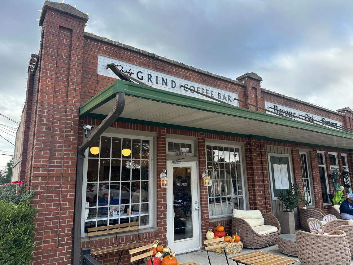 The brick exterior of the Daily Grind Coffee Bar. The building has large windows, a green awning, and outdoor seating with pumpkins for decoration.