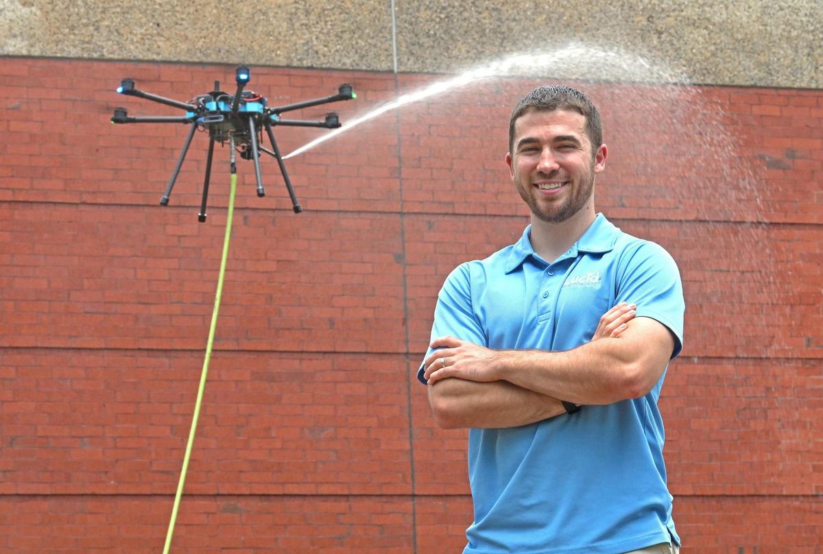 Andrew Ashur, CEO and founder of Lucid Drone Technologies in Charlotte, with one of the company’s drones cleaning a building in the background on Friday. Lucid Drone Technologies has built drones to clean buildings and windows.