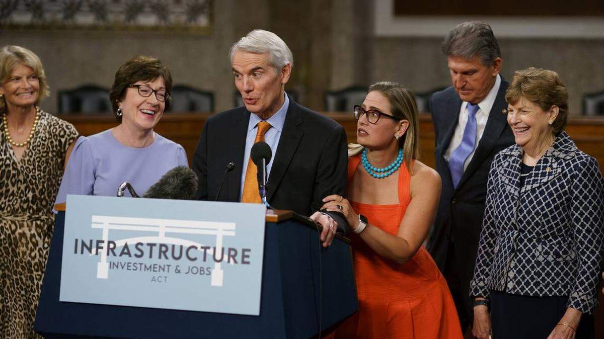 The bipartisan group of Senate negotiators speak to reporters July 28, 2021, just after a vote to start work on a nearly $1 trillion bipartisan infrastructure package. From left are Sen. Lisa Murkowski, R-Alaska, Sen. Susan Collins, R-Maine, Sen. Rob Portman, R-Ohio, Sen. Kyrsten Sinema, D-Ariz., Sen. Joe Manchin, D-W.Va., and Sen. Jeanne Shaheen, D-N.H.