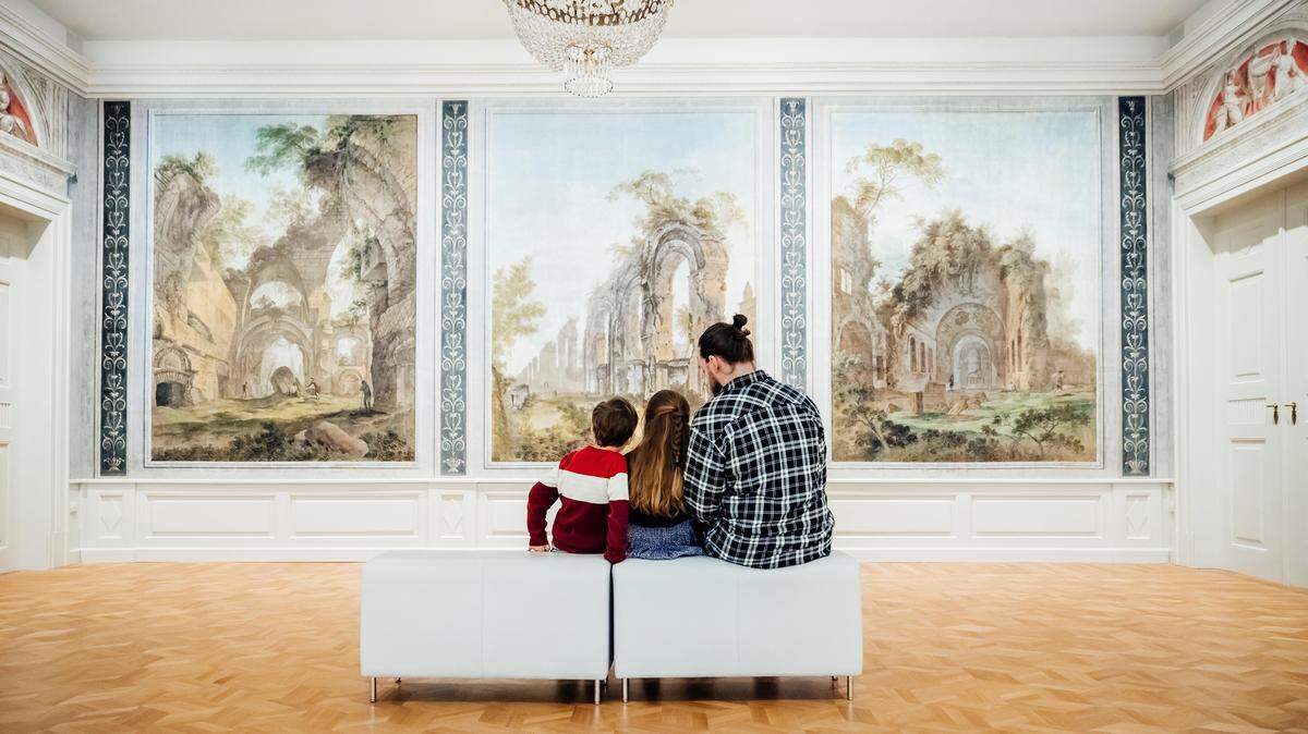 A single father sitting with his two young children and enjoying some paintings on display while visiting a museum together.