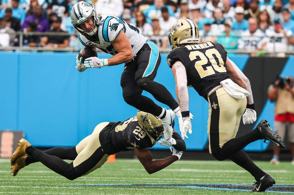 Panthers running back Christian McCaffrey, center, jumps through the grasp of Saints cornerback Paulson Adebo during the game at Bank of America Stadium on Sunday, September 25, 2022 in Charlotte, NC. McCaffrey became the first running back to notch consecutive 100-yard rushing games this season in the Panthers’ 22-14 victory.