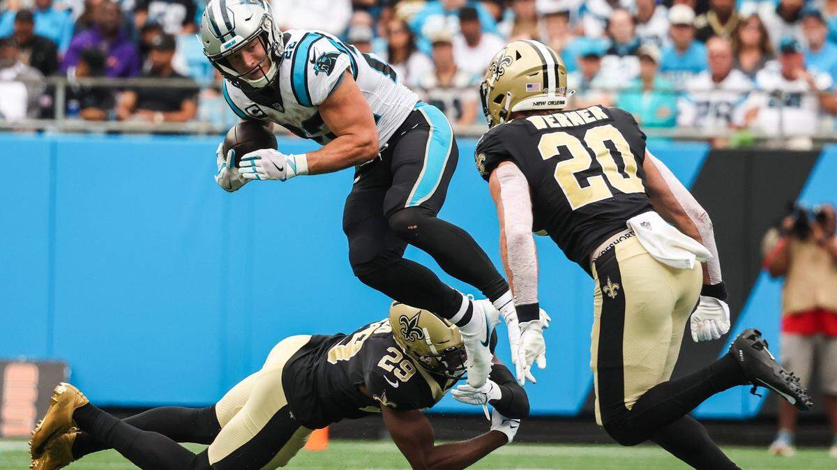 Panthers running back Christian McCaffrey, center, jumps through the grasp of Saints cornerback Paulson Adebo during the game at Bank of America Stadium on Sunday, September 25, 2022 in Charlotte, NC. The Panthers pulled out their first win of the season by defeating the Saints 22-14.