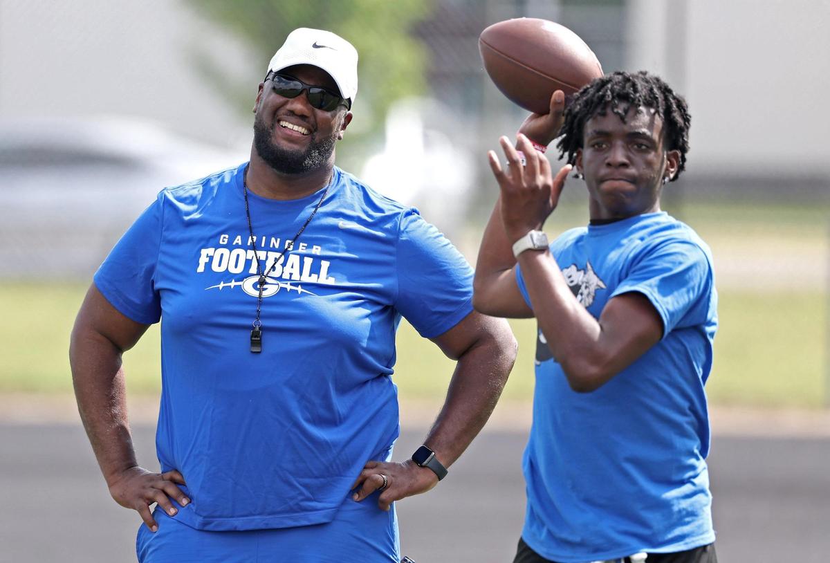 Garinger High School head football coach Jupiter Wilson, left, smiles as he watches one of the team’s quarterback’s pass during a workout on Tuesday, April 29, 2025. Garinger High School has been through dozens of coaches trying to turn the program around. Now, the former UNC football player is taking his turn.