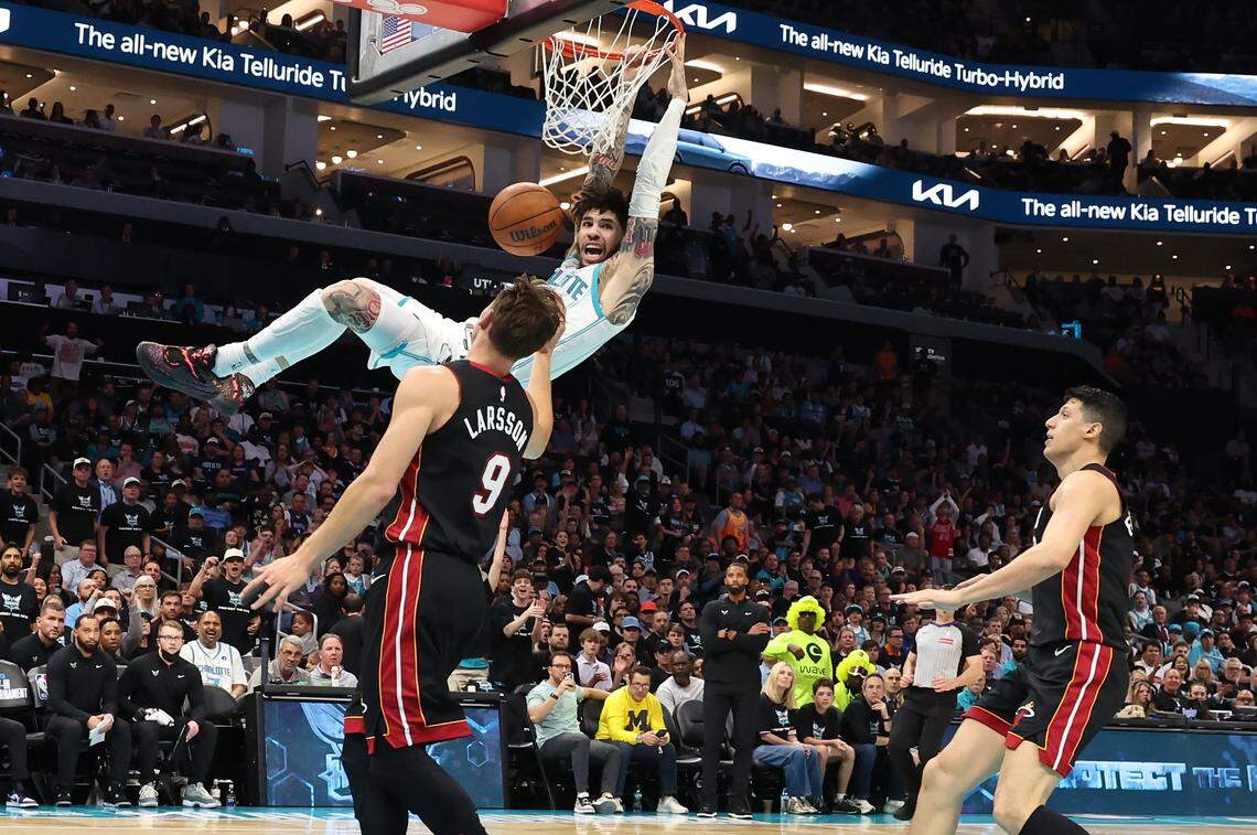 Charlotte Hornets guard LaMelo Ball, center, looks toward an official as he finishes off a two-handed dunk as Miami Heat forward Pelle Larsson, left and forward Simone Fontecchio, right, look on during action at Spectrum Center in Charlotte, NC on Tuesday, April 14, 2026. The Hornets defeated the Heat 127-126 in NBA Play-in-Tournament basketball game.