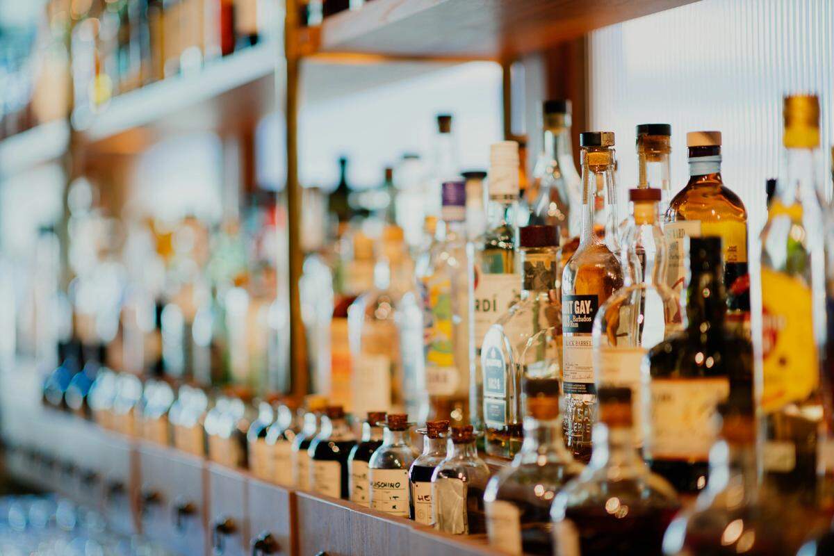 A bar shelf holds multiple rows of small glass bottles filled with various spirits. The bottles in the foreground are in focus, while the rest blur into the background.