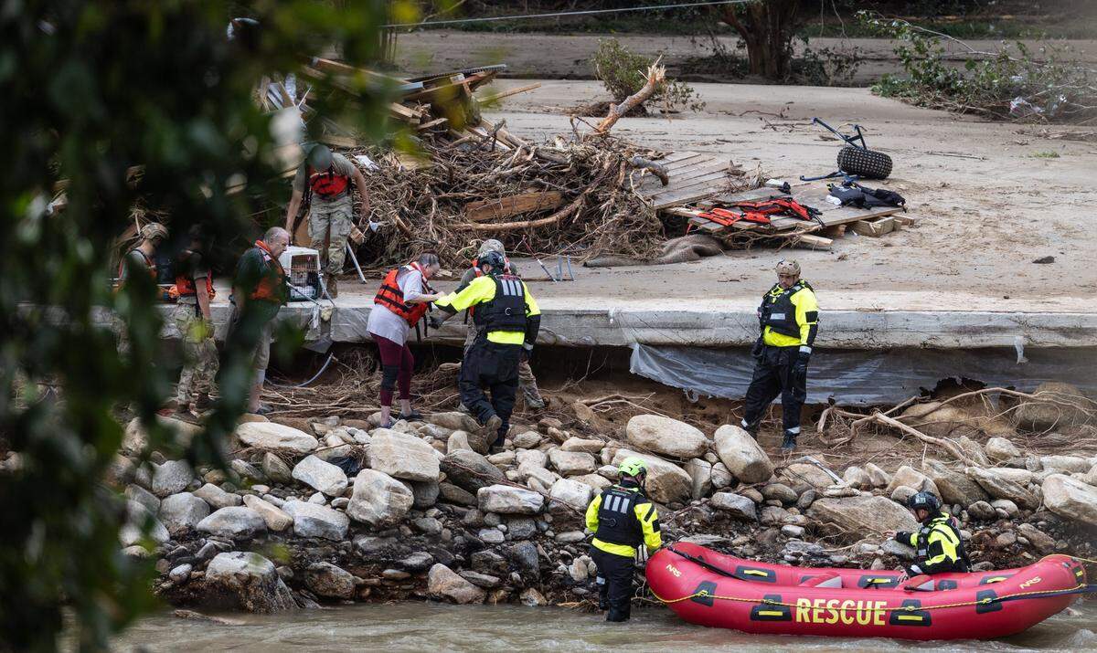 Two people and a dog are escorted to a rescue boat in Chimney Rock, N.C. on Sunday, September 29, 2024.
