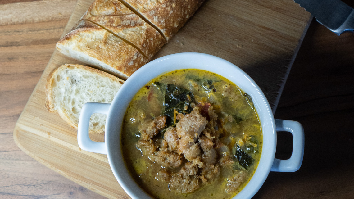 Italian wedding soup in a bowl placed near slices of bread.