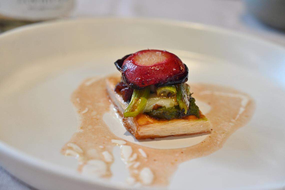 A balsamic bacon and plum tart tatin sits on a white plate.