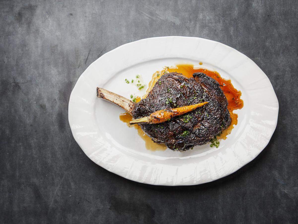 A high-angle, minimalist shot of a single plated steak against a dark, textured slate-gray background.