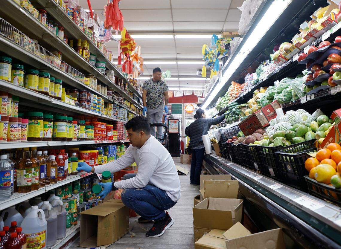 Erick Canales and Carlos Cruz Santiago stock shelves as Marielena Ortiz shops at Moroleon Supermarket on Friday, Oct. 21, 2022, in Durham, N.C.