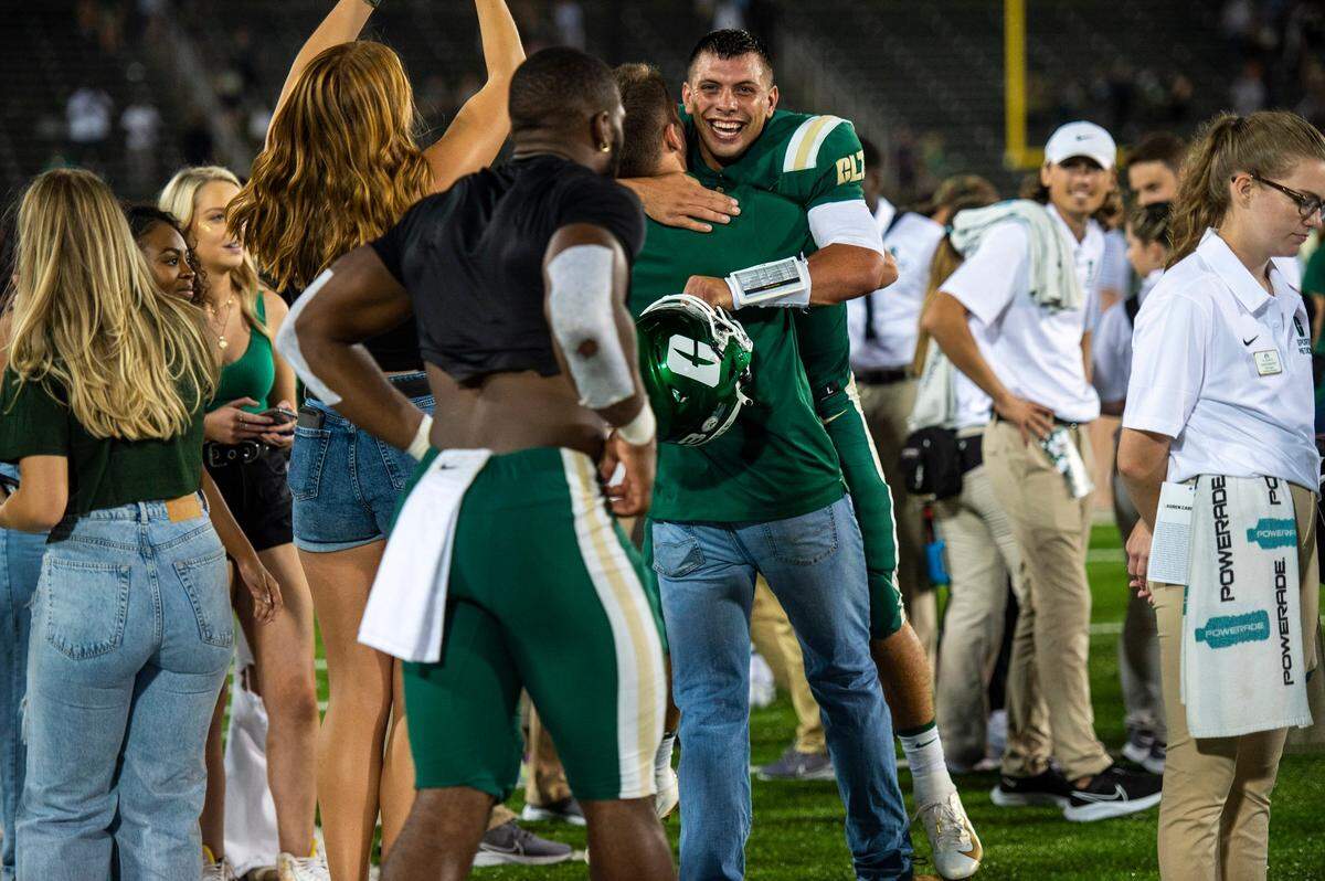 Charlotte 49ers quarterback, Chris Reynolds, back center, receives hugs when fans and students rushed the field after the 49ers win over the Duke Blue Devils at Jerry Richardson Stadium on Friday, September 3, 2021 in Charlotte, NC. Ahead of the season opener on Friday, UNC Charlotte officials announced game day protocols for fan safety. All spectators five years and older were encouraged to wear masks during the game against the Blue Devils. Officials say fans can pull down their masks when actively eating or drinking.