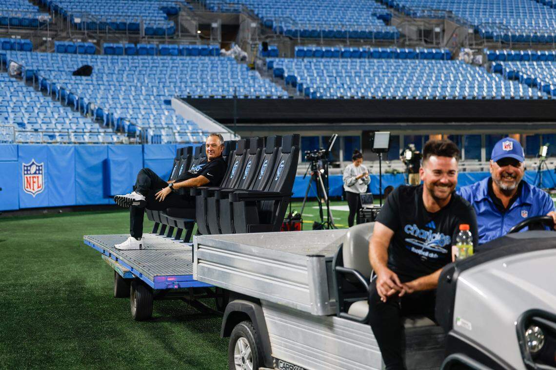 A worker catches a ride on a row of Charlotte FC seating used inside shelters for the MLS game this Tuesday night. Stadium operations crew work diligently to start transitioning the field from an NFL game, to an MLS game at Bank of America Stadium in Charlotte, NC on Sunday, October 26, 2025.