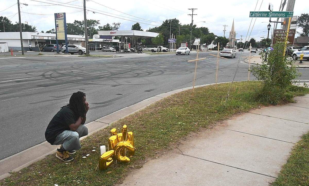 Timothy Moore kneels beside a memorial for shooting victims at the corner of Beatties Ford Road and Catherine Simmons Avenue. Moore lost his cousins, Christopher Antonio Gleaton and Kelly Miller, in gunfire that broke out at an outdoor party on June 22. Four people died in the shootout.